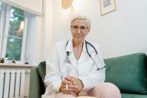 Kvinna i vit läkarrock med stetoskop sitter i en soffa vid en konsultation.