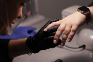 Närbild på en nagelterapeut med svarta handskar som gör manikyr på en kund.