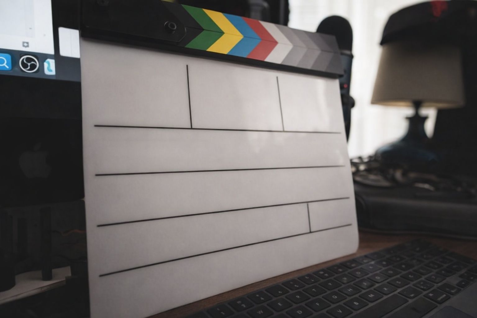 En vit filmklappa står på ett skrivbord framför en datorskärm.